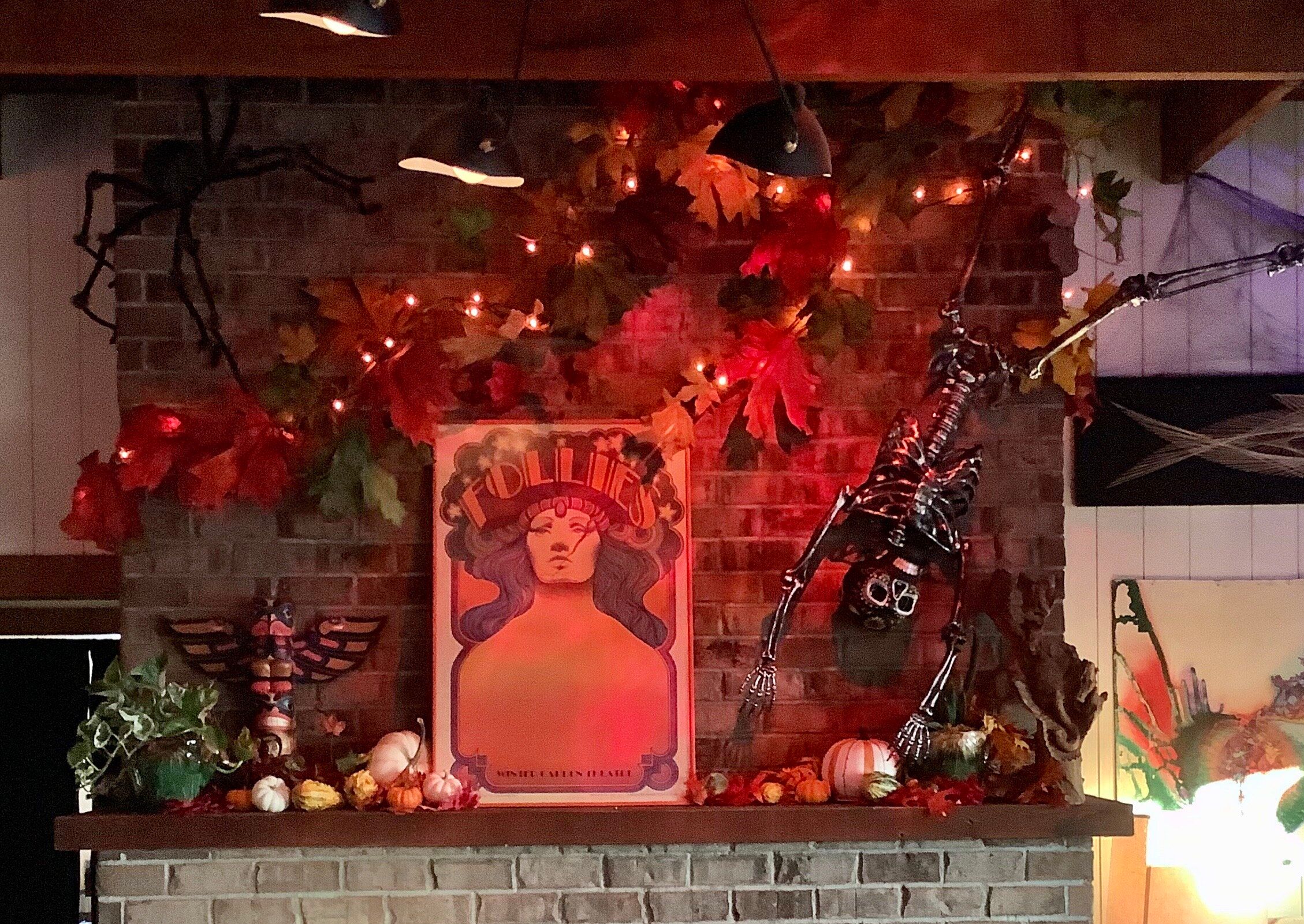 A mantel decorated for Halloween with a skeleton, string lights and fall leaves